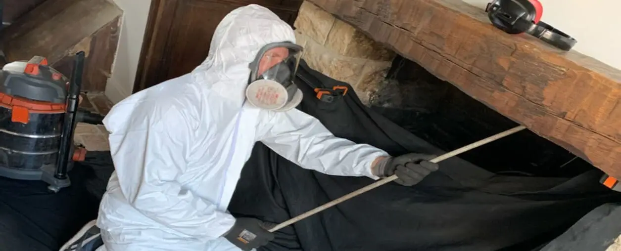 Professionnel en combinaison et masque de protection débistrant un conduit depuis le foyer d'une cheminée