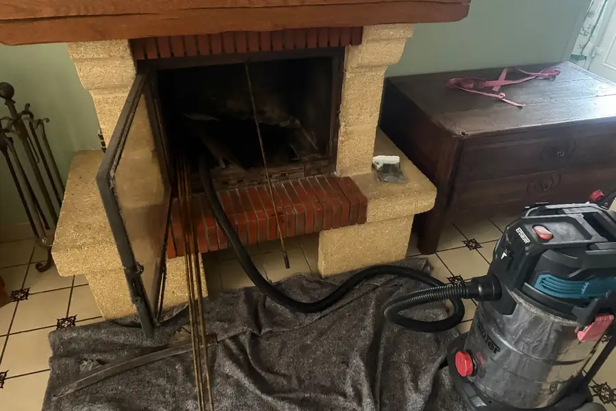 Ramonage d'un insert par le bas : cannes de ramonage dans le foyer, sol protégé par une couverture et aspirateur prêt