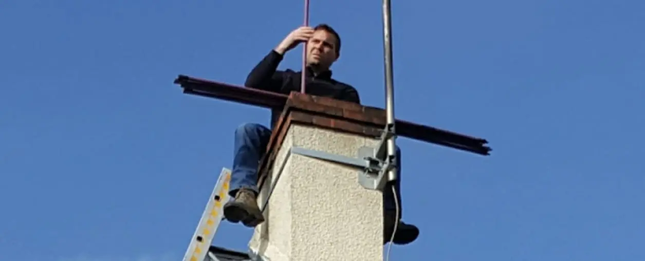Ramoneur assis sur une souche de cheminée pendant un ramonage par le toit